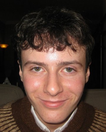 Enzo smiling in a brown knit sweater with a white collar